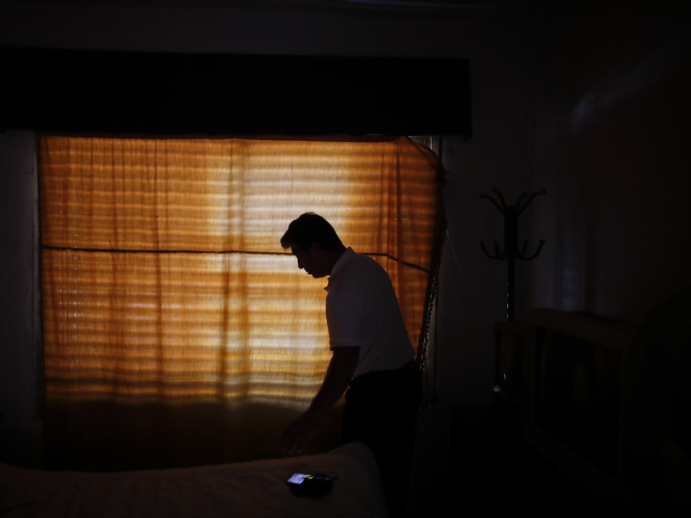 Claudio Rojas, who was deported from the U.S. in 2019, is silhouetted against a curtained window of his home in Moreno, Argentina, on May 8, 2021. He was able to return to the U.S. in August.