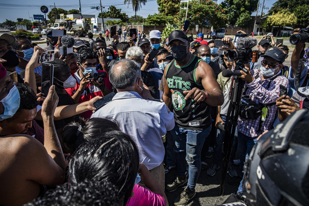 Cuban Heidel Roberto, right, complains to Hugo Salvador Cuéllar of the INM about the lack of buses. The slow deployment of northbound buses has frustrated many Haitians and other migrants who are unhoused in Tapachula.