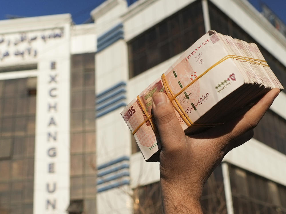 An Afghan money changer holds a stack of Iranian currency at Khorasan market in Herat, Afghanistan, The value of Afghanistan's currency is tumbling, exacerbating an already severe economic crisis.