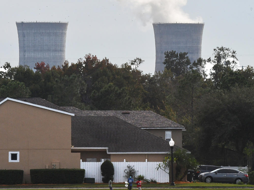 The cooling towers at the Stanton Energy Center, a coal-fired power plant, are seen behind a home in Orlando.