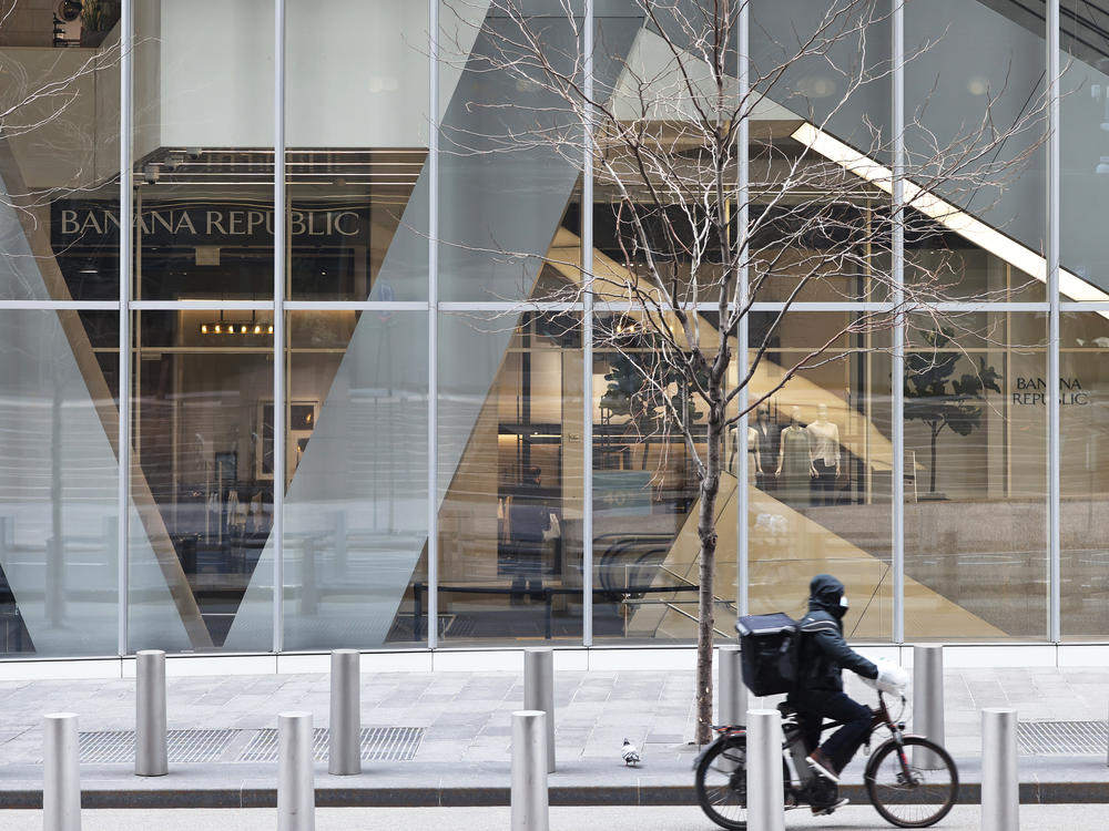 A delivery person rides a bicycle past a storefront in New York City.