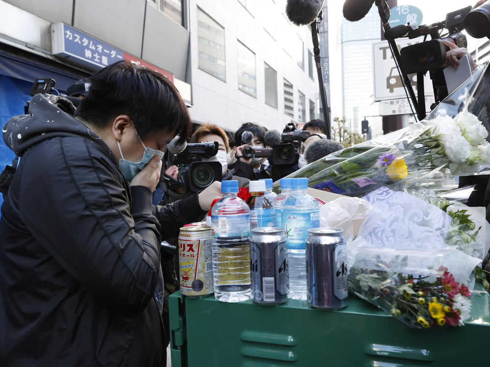 A mourner offers a flower on Saturday near the building where a fire broke out the day before in Osaka, western Japan. The fire spread from a fourth-floor mental clinic in the eight-story building in downtown Osaka and killed more than 20 people in what police were investigating as a possible case of arson and murder.