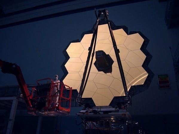 The James Webb Space Telescope's primary mirror is illuminated inside a darkened clean room. The entire telescope is now packed inside a rocket, awaiting launch.