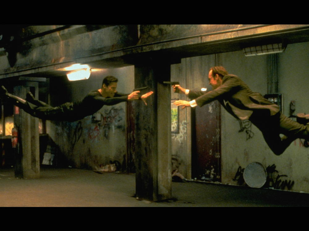 Keanu Reeves and Hugo Weaving face each other in a scene from The Matrix.