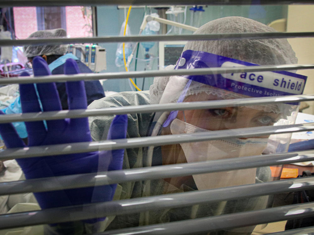 Respiratory therapist Miriah Blevins peers out a window looking for assistance as she cares for a patient. When staffers are wearing personal protective equipment in a sealed room, they often need help.