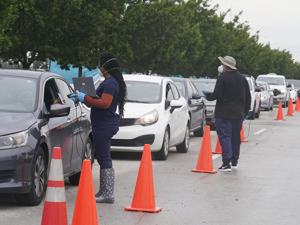 Employees of Nomi Health check in a long line of people for COVID-19 tests on Tuesday in North Miami, Fla.