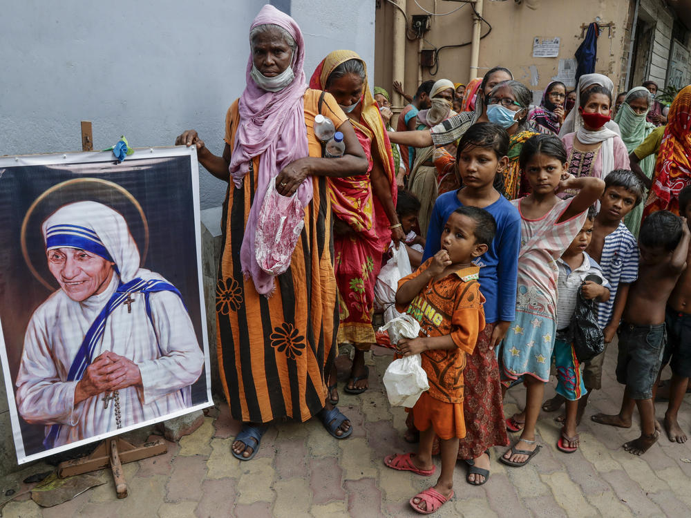 Homeless people gather beside a portrait of Saint Teresa, the founder of the Missionaries of Charity, to collect free food outside the order's headquarters in Kolkata, India, in August.