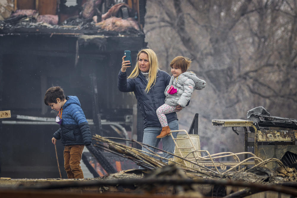 Kennedy Reynolds, standing with her daughter Belle, 2, and son Forrest, 6, takes a photo of a burned-out condo in Louisville, Colo., on Friday.