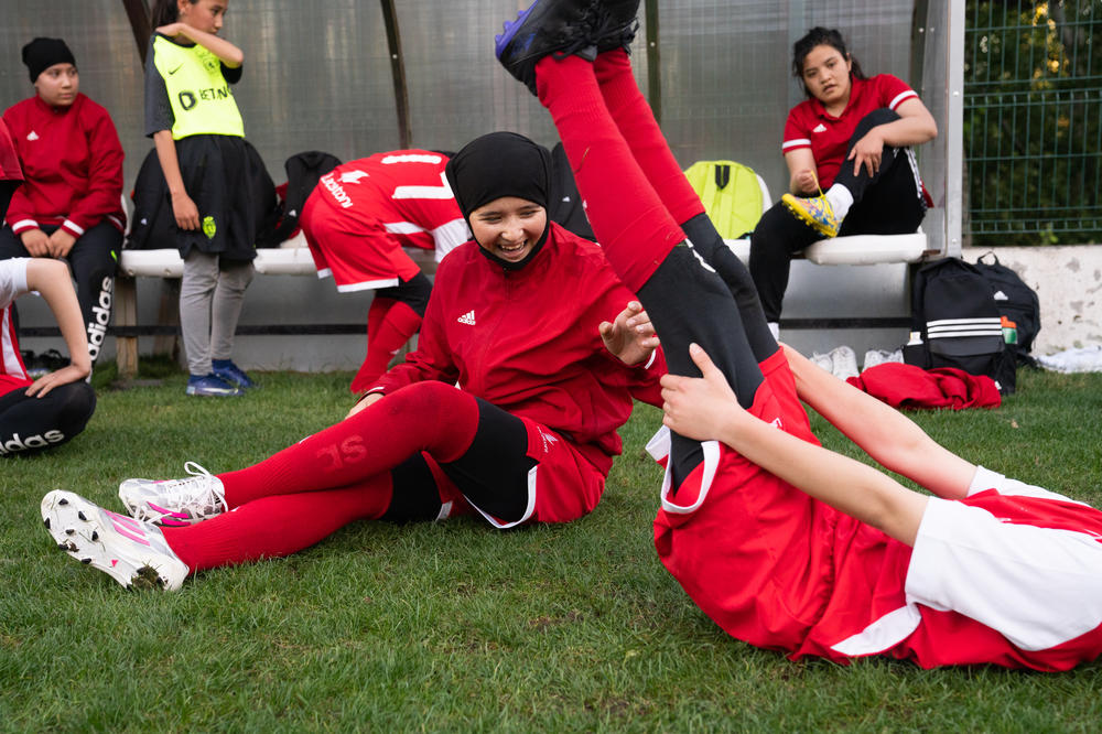 The girls laugh and stretch together during a break from soccer practice.