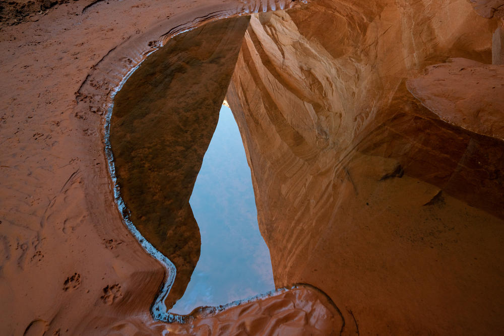 Reflections of cliffs appear in a small puddle of water where the water used to be very deep, near Cathedral in the Desert, a monument in Glen Canyon.