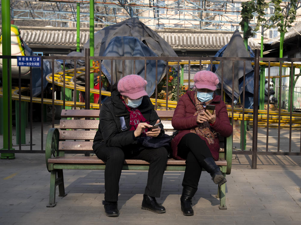 Women wearing face masks to protect against COVID-19 look at their smartphones at a public park in Beijing Wednesday. China is reporting a major drop in local COVID-19 infections in the northern city of Xi'an, which has been under a tight lockdown for the past two weeks.