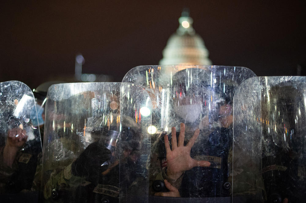 National Guard troops bearing shields clear a street from protesters outside the Capitol building that evening.
