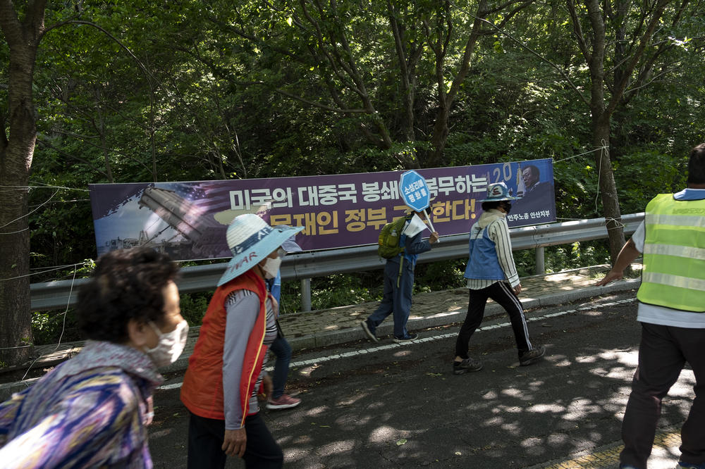 Protesters march toward the entrance of a U.S. and South Korean base where a missile defense battery is deployed. Behind them, a poster made by a local labor union reads: 