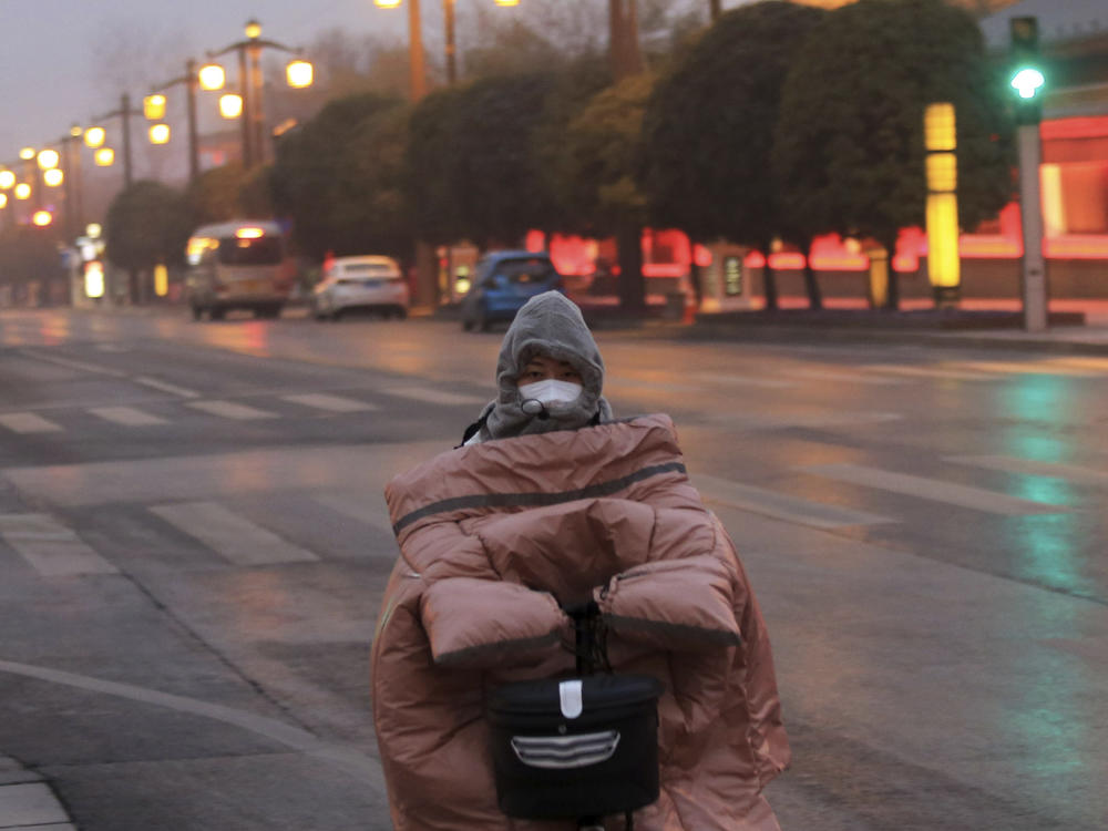 A woman wearing a face mask to protect against COVID-19 rides down a mostly empty street in Xi'an in northwestern China's Shaanxi Province, Thursday, Jan. 6, 2022.