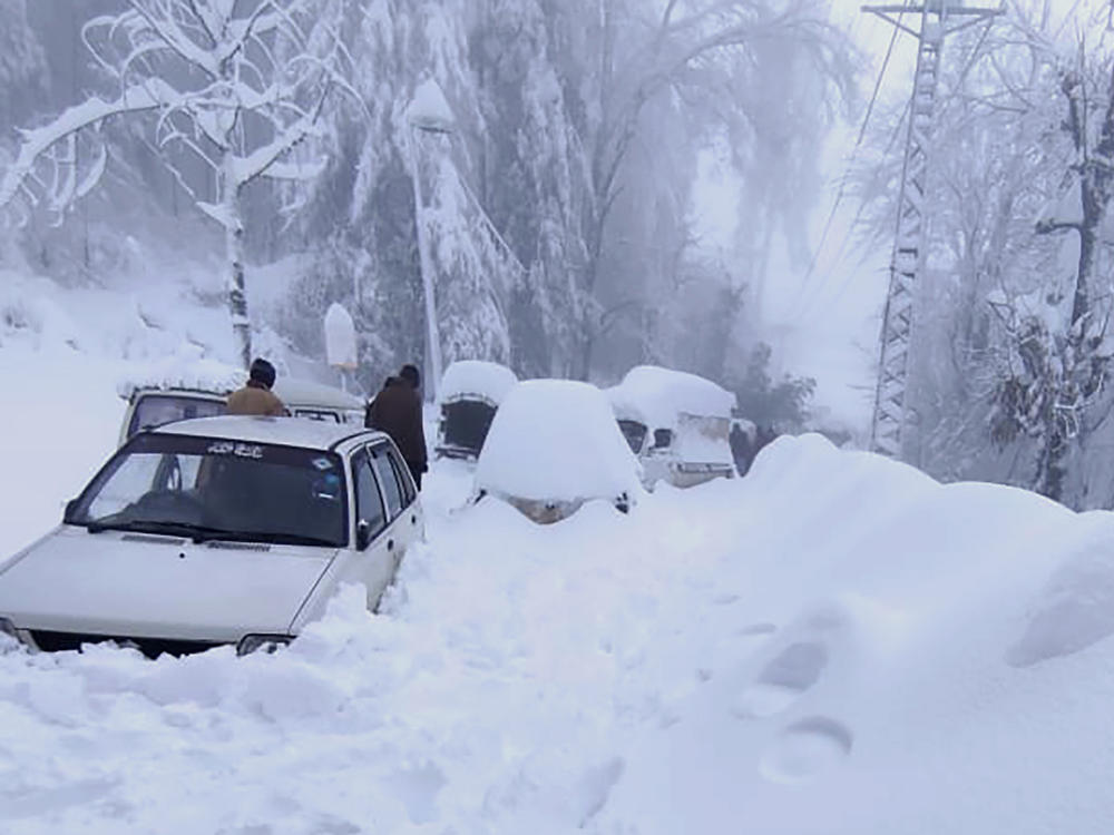People walk past vehicles trapped in a heavy snowfall-hit area in Murree, some 28 miles north of the capital of Islamabad, Pakistan, on Saturday.