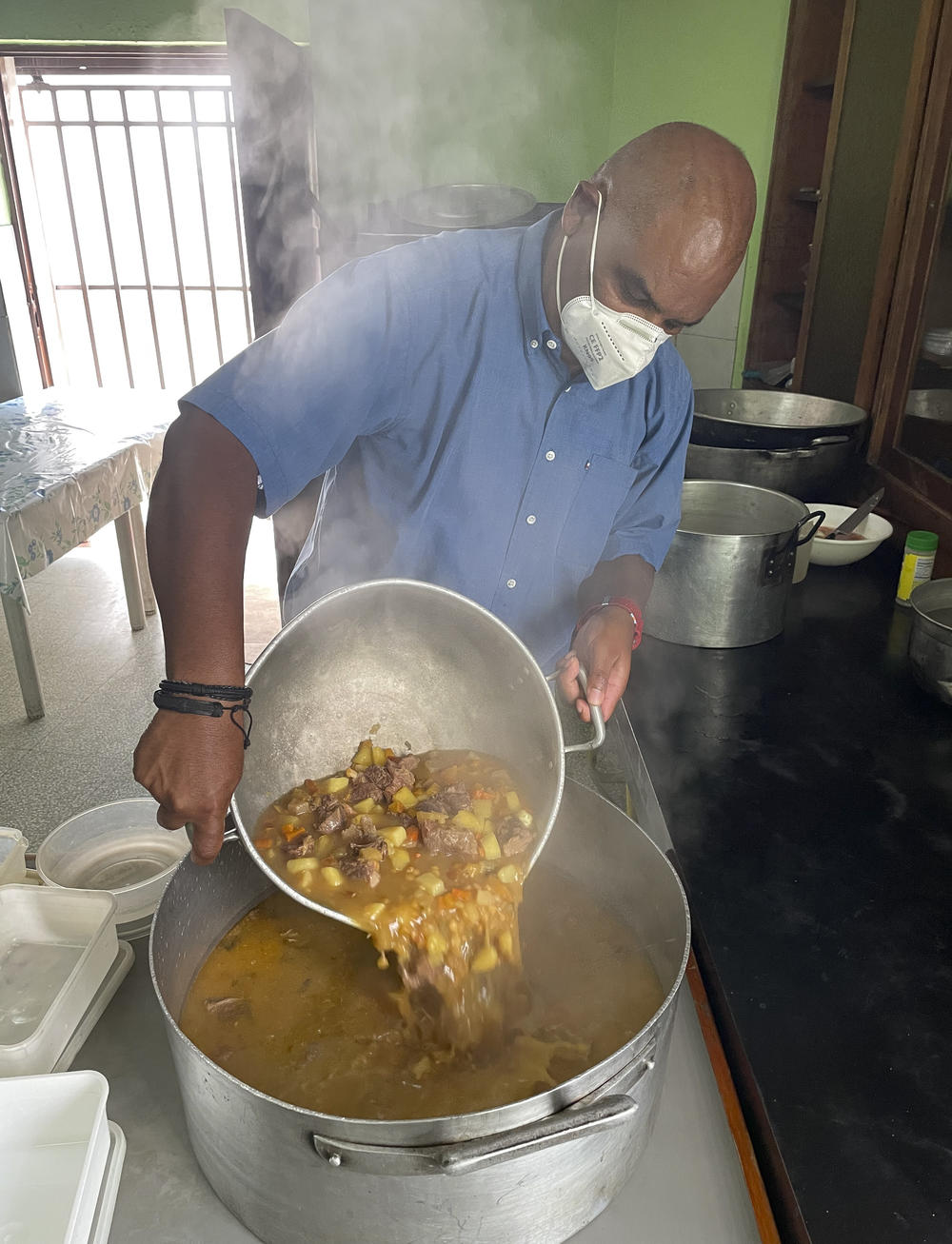A cook pours beef stew into a large container for distribution to malnourished people.