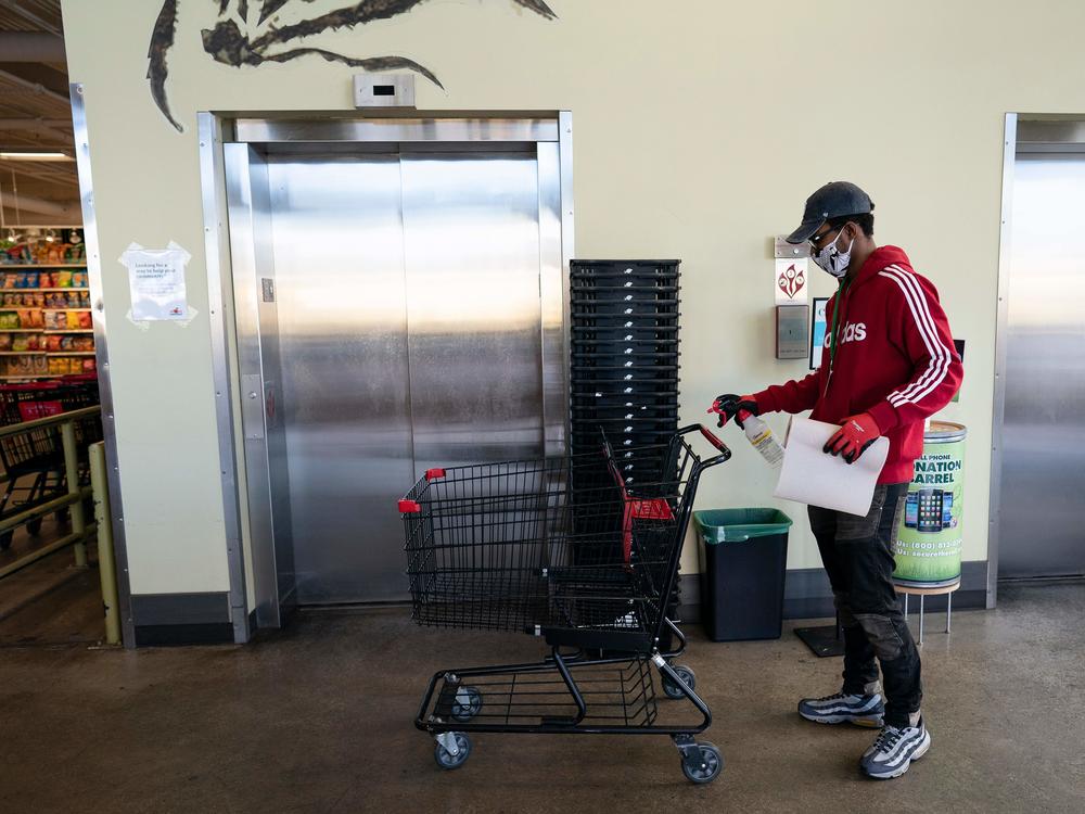 A grocery store worker sanitizes a shopping cart at a MOM's Organic Market in Washington, D.C., in April 2020.