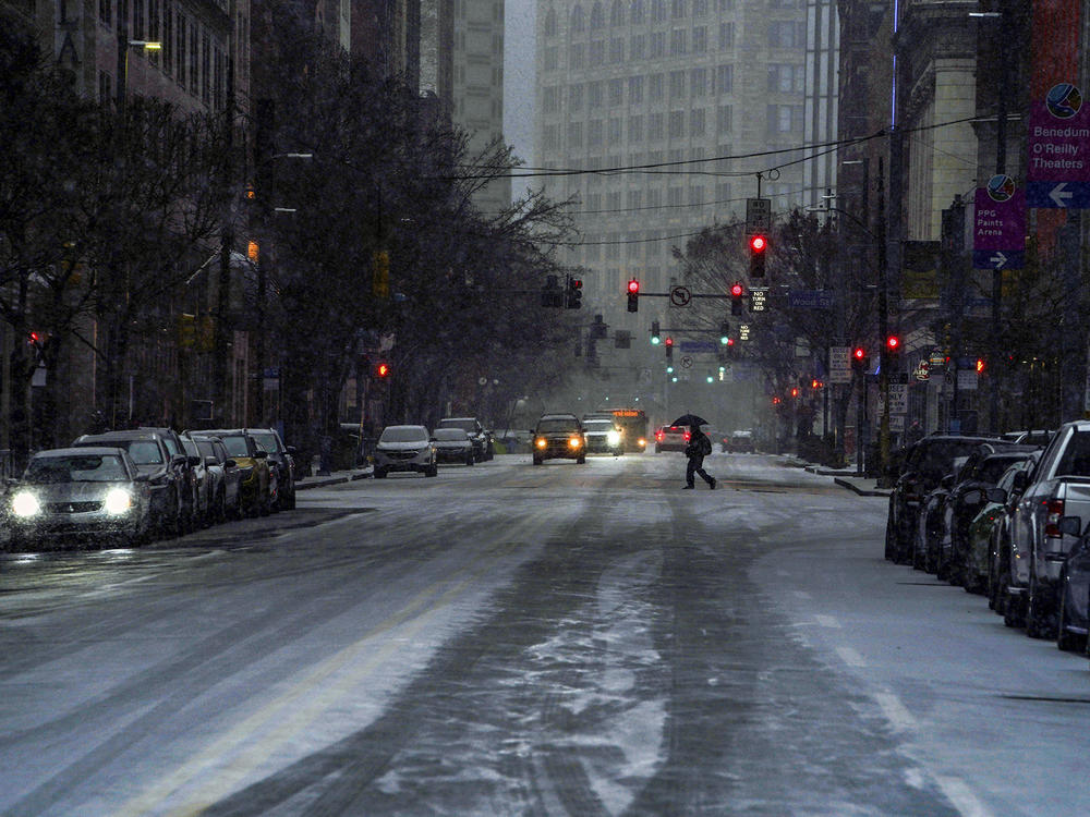A pedestrian uses an umbrella as they cross Liberty Avenue, in downtown Pittsburgh, as snow begins to fall during a winter storm that will impact the region on Sunday night, Jan. 16, 2022.