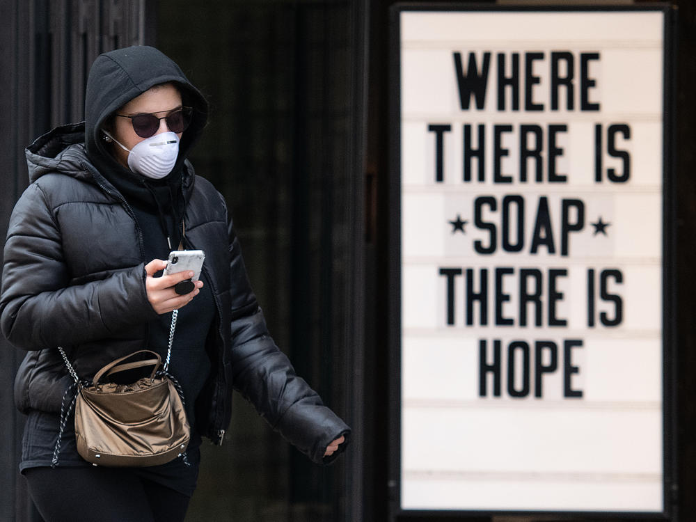 A woman wearing a protective mask walks past a sign in a cosmetic shop window on March 17, 2020 in London, England.