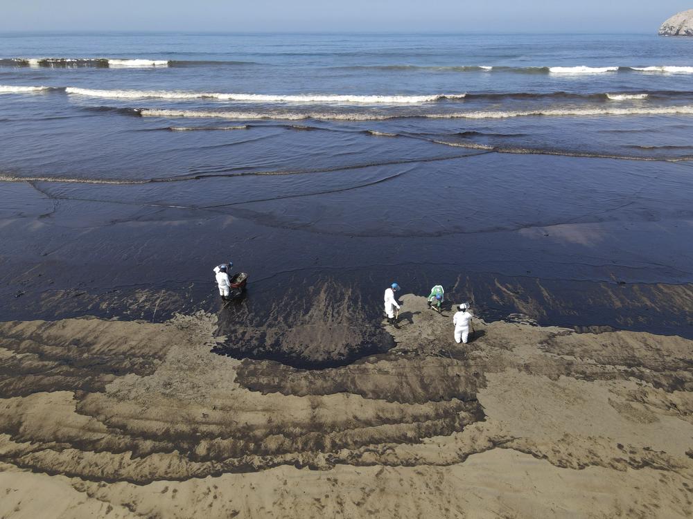 Workers clean up oil from Cavero beach on Tuesday.