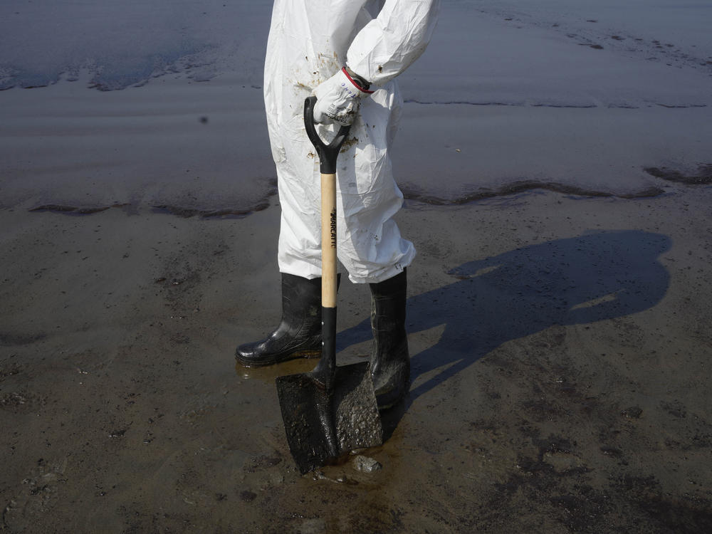 A worker pauses on Cavero beach during the cleaning away of oil on Tuesday.