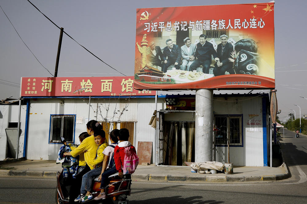 A Uyghur woman rides past a billboard showing China's president, Xi Jinping, joining hands with a group of Uyghur elders at the Unity New Village in Hotan, in the Xinjiang region, in 2018.