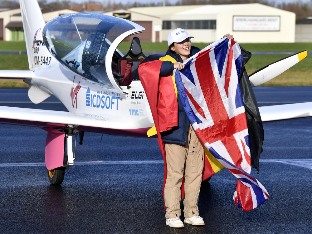 Zara Rutherford, 19, carries the Belgian and British flags on the tarmac after landing her Shark ultralight plane at the Kortrijk airport in Belgium, on Thursday at the completion of a record-breaking solo circumnavigation.