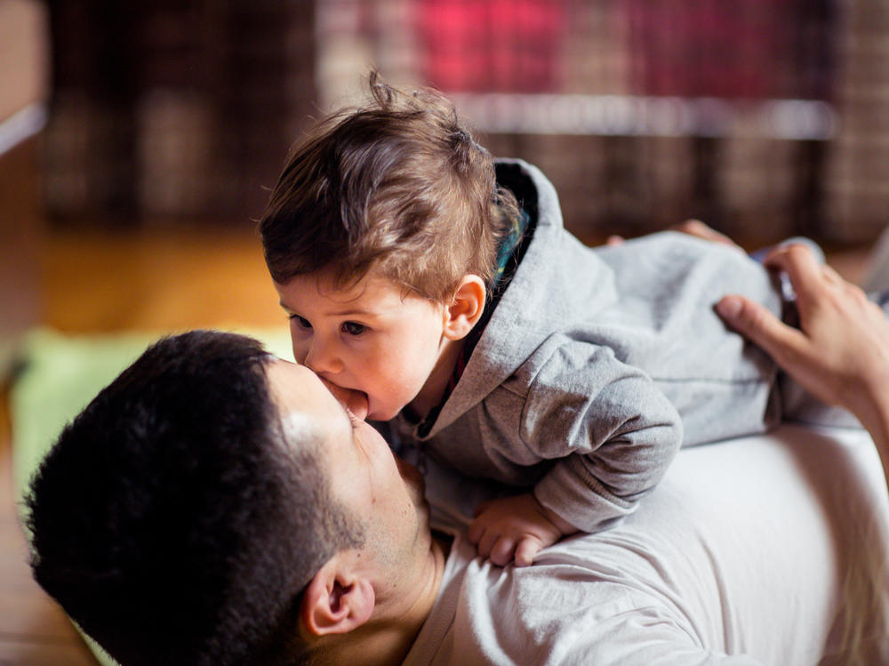 This stock image shows a baby and father playing at home. New research finds that babies judge the relationship between two people by whether or not they willingly share saliva.
