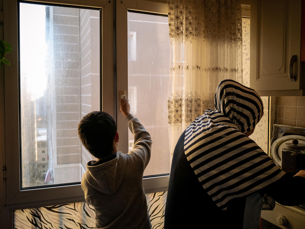 Lütfullah stands behind his stepmother, Neriman Kuçar, in their kitchen in Istanbul. She made the children <em>laghman</em>, Uyghur-style noodles, and Aysu cried. She was served Uyghur food only twice while she was at the state boarding school, but both times older classmates ate it all before she could take a bite.