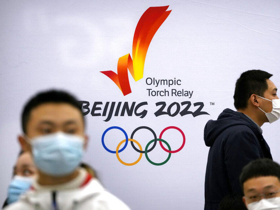 Participants wearing face masks gather near a logo for the 2022 Winter Olympic torch relay during an event to display the Olympic torch and flame at the Beijing University of Posts and Communications in Beijing, Thursday, Dec. 9, 2021.