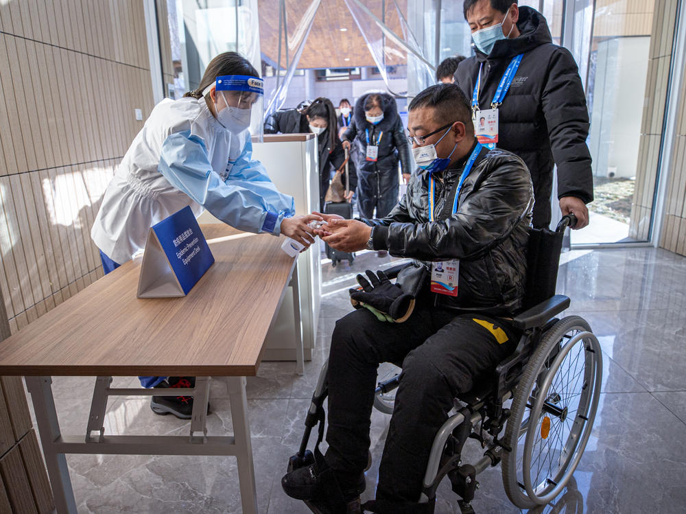 In a test of procedures to prevent transmission of COVID, a volunteer disinfects the hands of participants at the Winter Olympics athletes' village late last year.