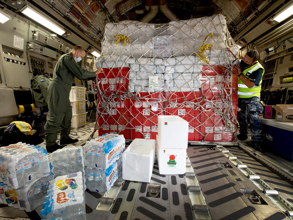Air Force Load Master Corporal Dale Hall (left) helps secure humanitarian aid supplies for Tonga aboard an Australian aircraft.
