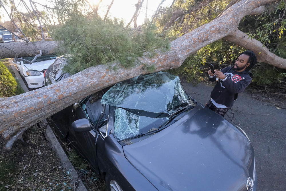 Brandon Crenshaw takes photos as a fallen tree sits on top of his car after strong winds in Upland, Calif., on Saturday.