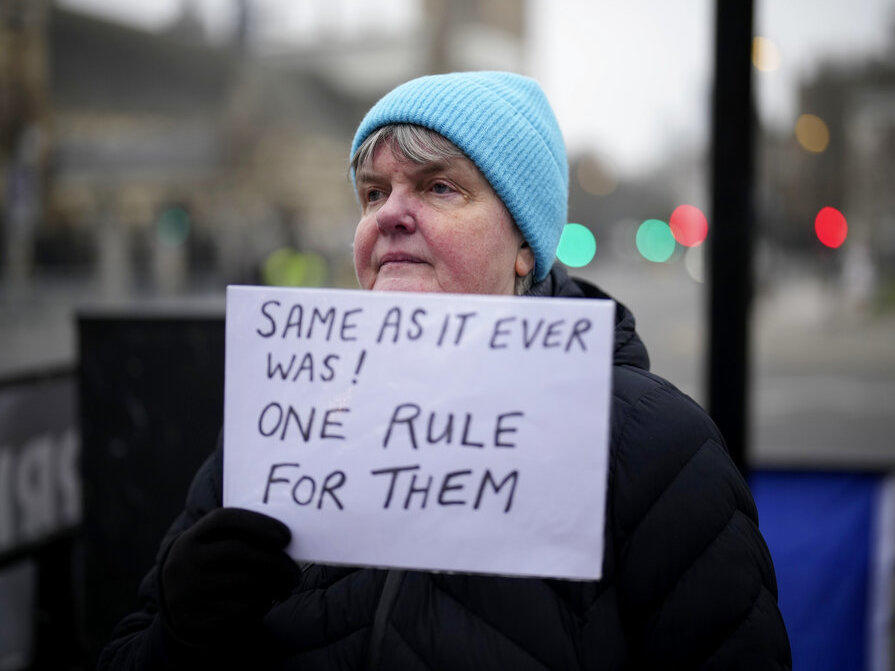 An anti-Brexit protester holds up an anti-government placard by Parliament Square, in London, Tuesday, Jan. 25, 2022.