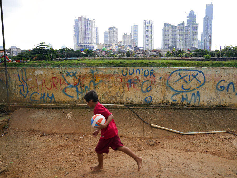 A young boy plays as high rise buildings at the main business district are seen in the background, in Jakarta, Indonesia, Tuesday, Jan. 25, 2022.