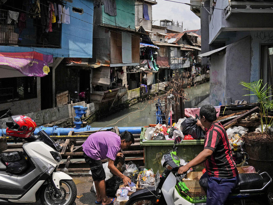 Men put garbage bags into an open dumpster in a low-income neighborhood in Jakarta, Indonesia, Tuesday, Jan. 25, 2022.