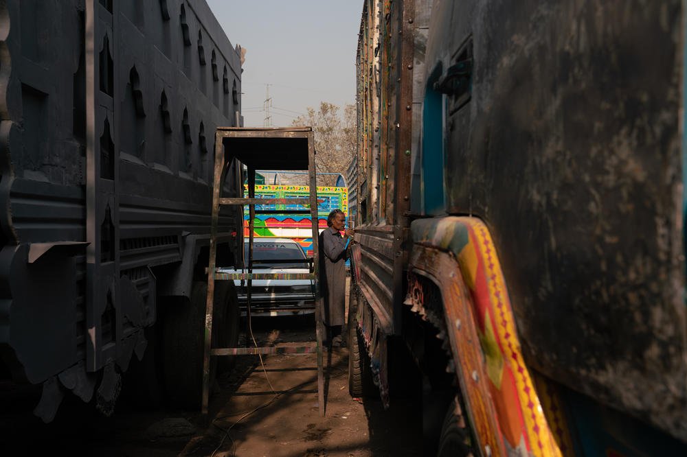 In a Rawalpindi truckyard, the trucks are lined up next to each other awaiting the attention and repairs of the mechanics and artists working there.