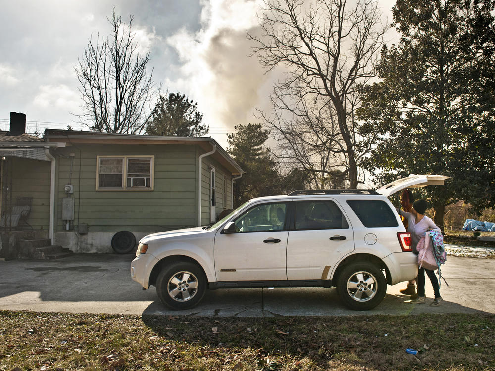 Smoke billows in the background as Chakona and Chayla Freeman pack up a car to evacuate their grandmother, Alice Pell, from her home in Winston-Salem on Tuesday. Pell's house is very near the Winston Weaver Co. fertilizer plant that caught fire Monday night.