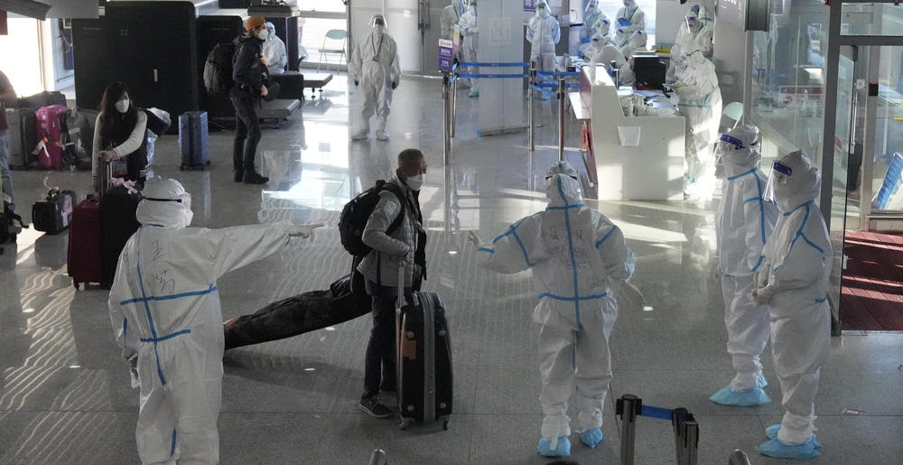 Chinese workers in protective suits at the Beijing airport guide arriving passengers ahead of the 2022 Winter Olympics, which formally begin on Friday.