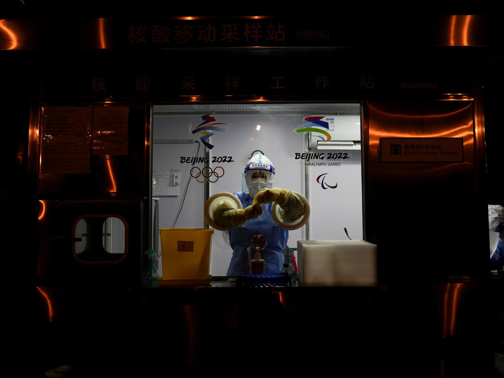 A worker prepares to administer a COVID-19 test at the 2022 Winter Olympics on Wednesday. So far, 111 athletes and officials have tested positive for the virus at the Olympics, including from people arriving at the airport.