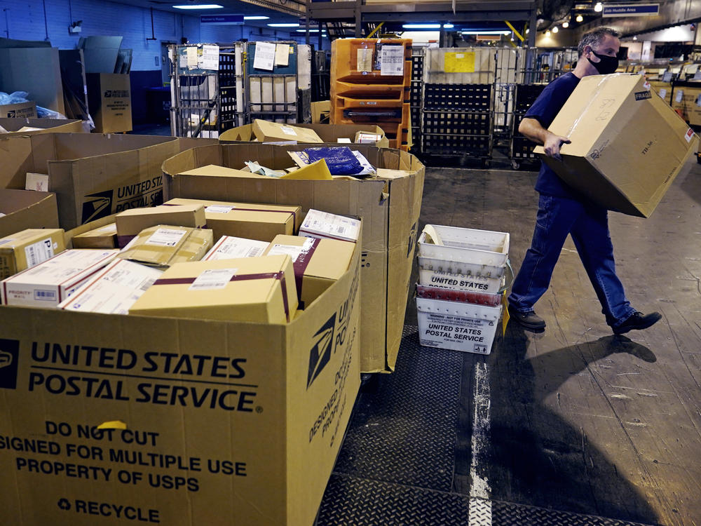 A worker carries a large parcel at the U.S. Postal Service sorting and processing facility in Boston on Nov. 18, 2021.