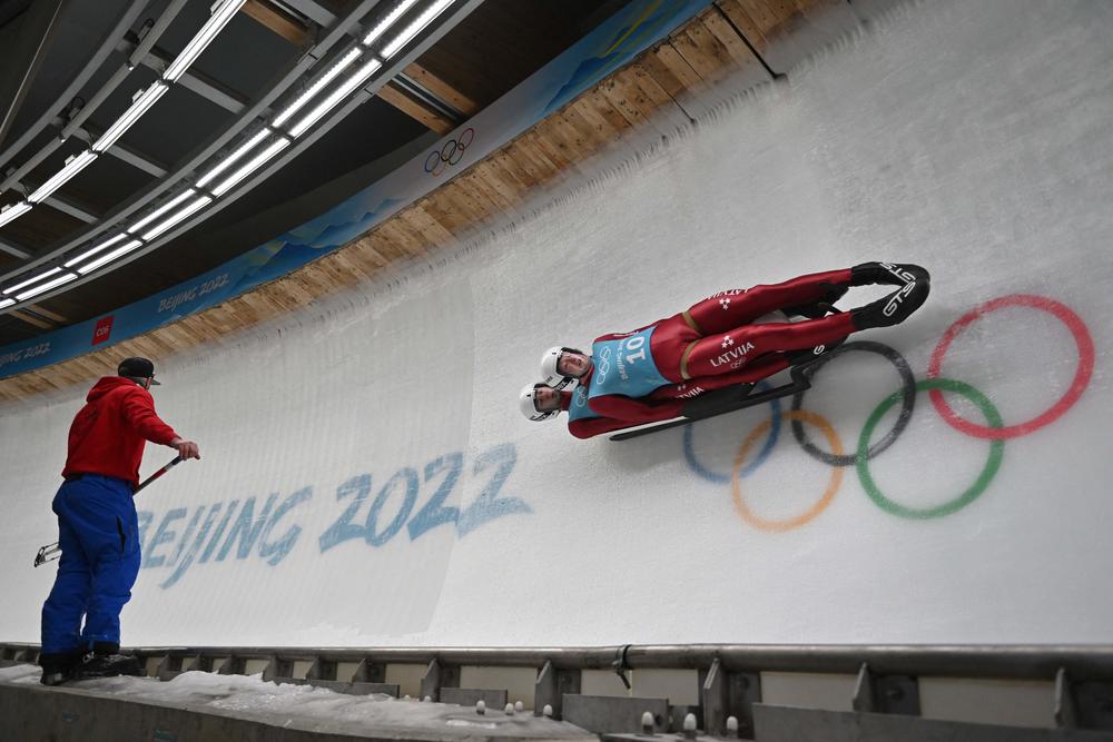 Latvia's Martins Bots and Roberts Plume take part in luge doubles training, as a track worker looks on, at the Yanqing National Sliding Centre during the Beijing 2022 Winter Olympic Games in Yanqing on February 6, 2022.