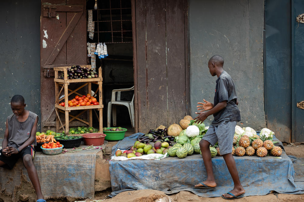 Kusemererwa Jonathan Henry, right, works at the fruit stand he started after school closed during the pandemic. 