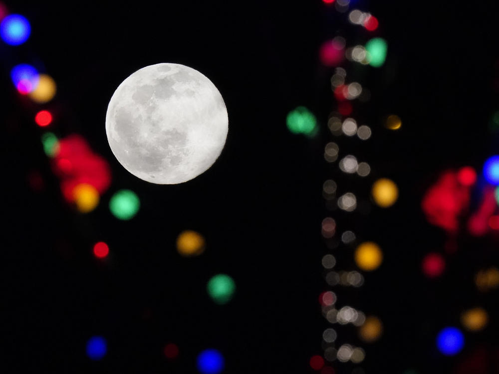 The full moon rises above strings of lights at the Olympic Green during the 2022 Winter Olympics on Wednesday in Beijing.