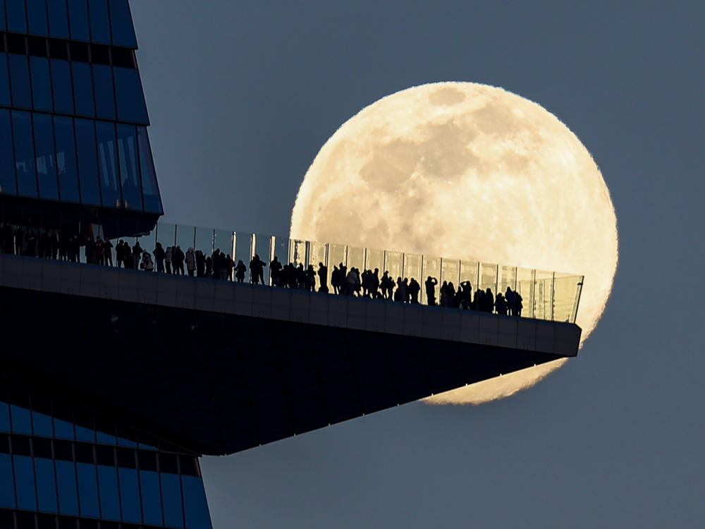 The moon rises on Tuesday behind people standing on The Edge, the outdoor observation deck in Manhattan.