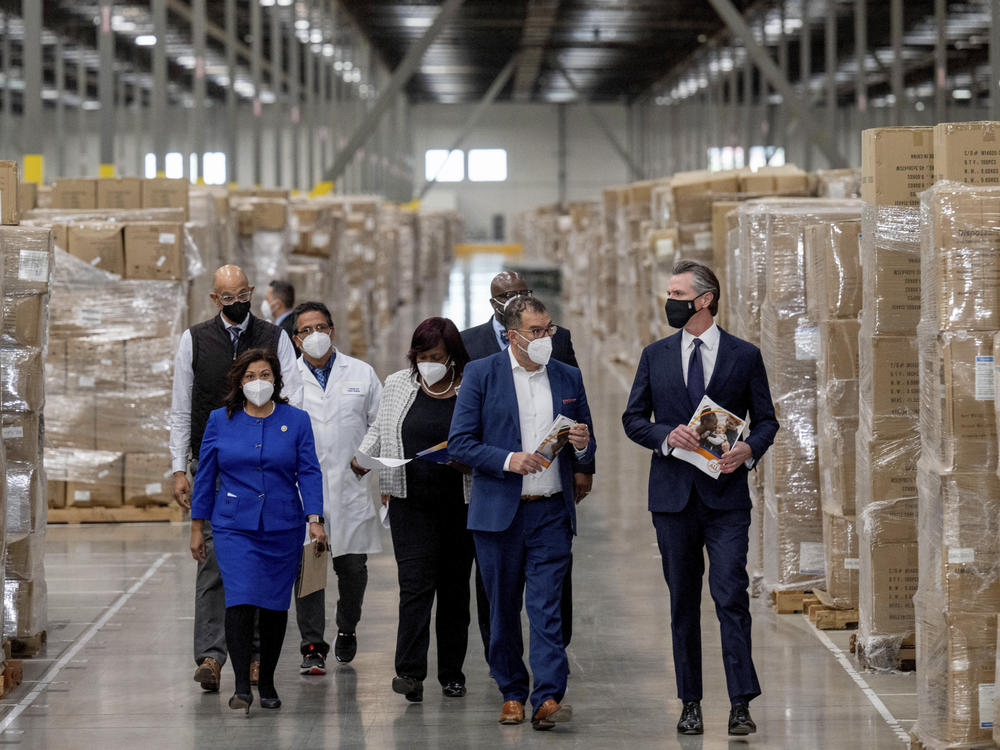 Gov. Gavin Newsom, right, walks through rows of boxed personal protective equipment with dignitaries and elected officials, as he prepares to announce the next phase of California's COVID-19 response on Thursday.