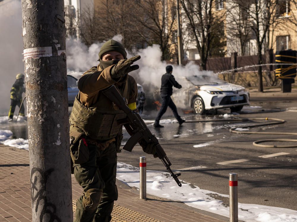 Ukrainian soldiers take positions outside a military facility as two cars burn in a street in Kyiv, Ukraine, on Saturday.