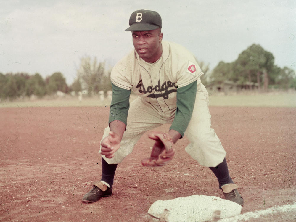 American professional baseball player Jackie Robinson of the Brooklyn Dodgers, dressed in a road uniform, crouches by the base and prepares to catch a ball in 1951.