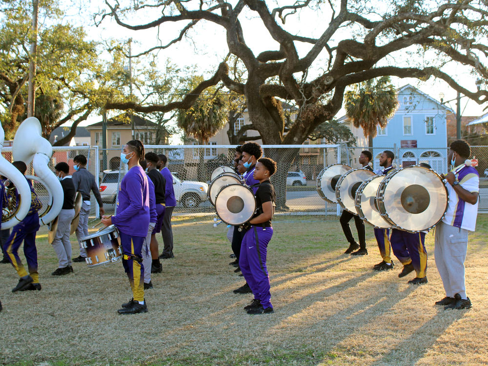 Warren Easton Charter High School's marching band members line up in formation. Their instruments, among many, include sousaphones, cymbals, and a drum section with snare, tenor and bass drums.