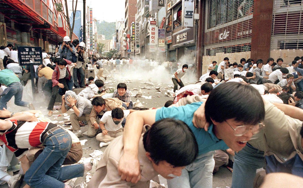 Anti-government protesters staging a sit-down strike in the center of Seoul, June 14, 1987, scatter in panic as tear gas grenades hurled by police explode.
